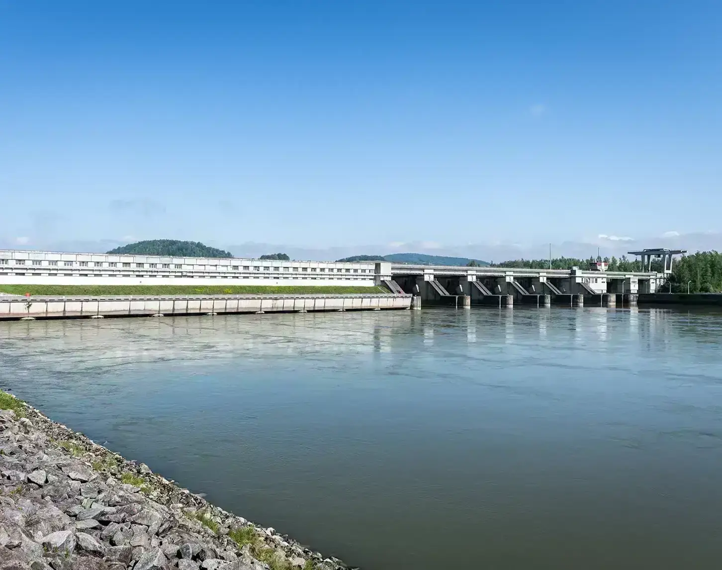 View of the Abwinden Asten power station. On the left you can see part of the riverbank. The blue sky is reflected in the Danube.